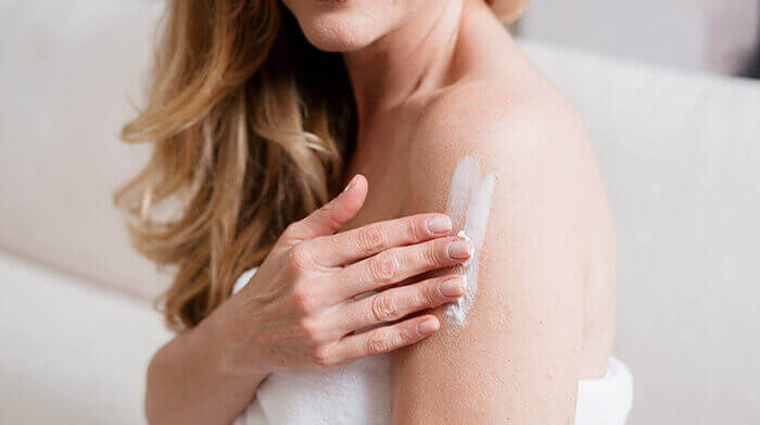 femme s'appliquant une épaisse couche de crème hydratante sur le bras