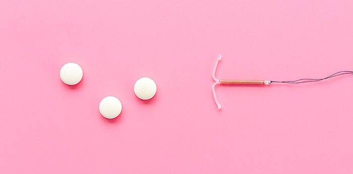 sterilet et pilules contraceptives sur fond rose