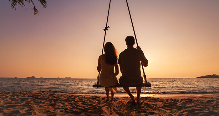 coiple sur une balançoire sur la plage au coucher du soleil