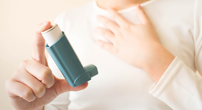femme tenant un bronchodilatateur en se tenant la poitrine
