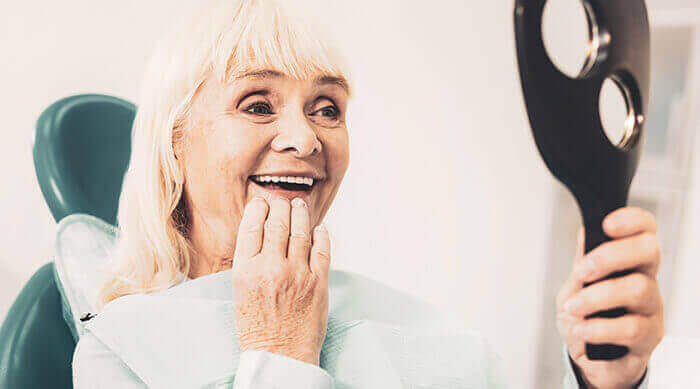 femme sénior qui observe ses dents dans un miroir