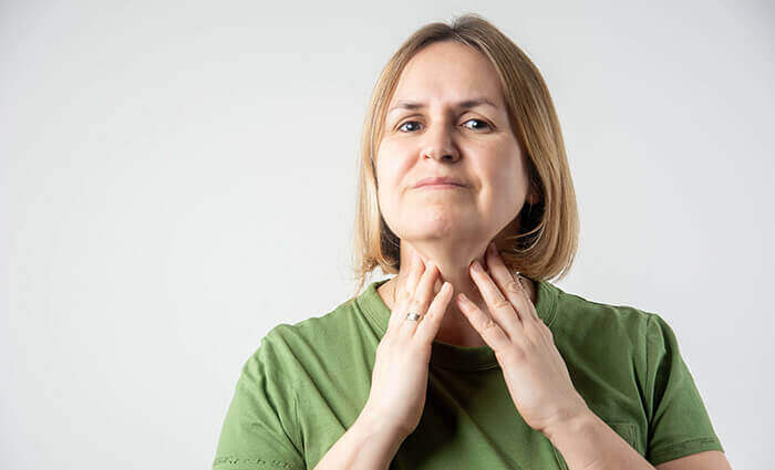 femme d'une cinquantaine d'année se tenant le cou au niveau de la thyroïde