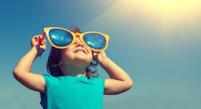 enfant faisant face au soleil avec des lunettes de soleil surdimensionnées