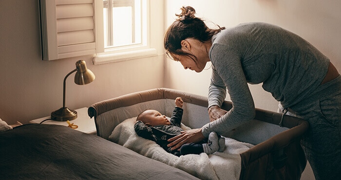 jeune maman qui couche son bébé dans un berceau de cododo