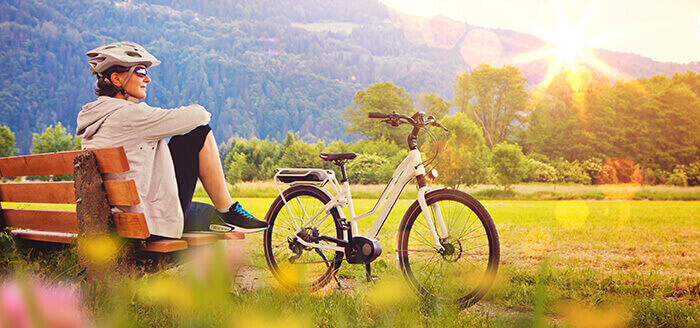 femme en pleine nature admirant un coucher de soleil, assise à côté de son vélo électrique dans le cadre d'une balade