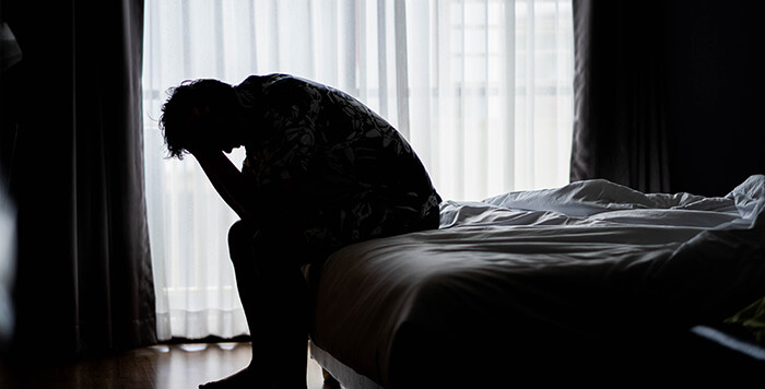 homme insomniaque assis sur le bord de son lit en se tenant la tête dans les mains