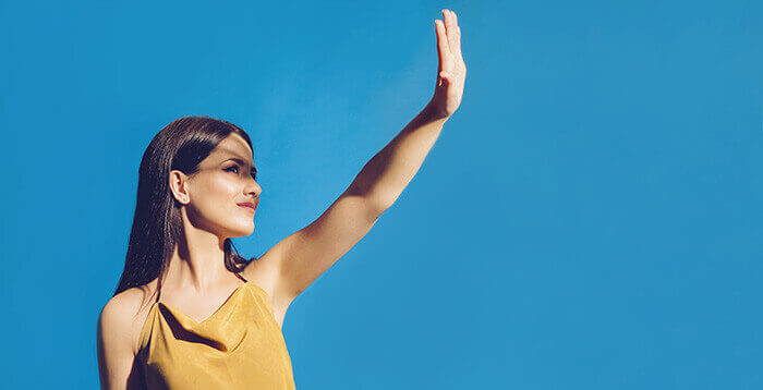femme se protegeant la peau du visage contre le soleil en tendant le bras