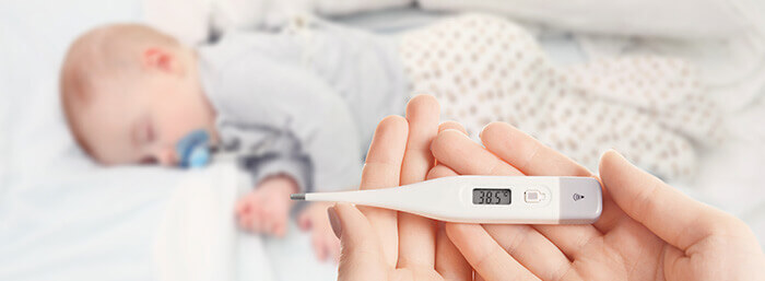 thermomètre indiquant une température de 38,5° chez un bébé dormant en arrière plan