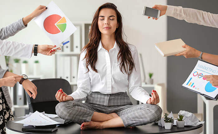 femme en position zen sur son bureau, resistant aux multiples solicitations stressantes de son travail