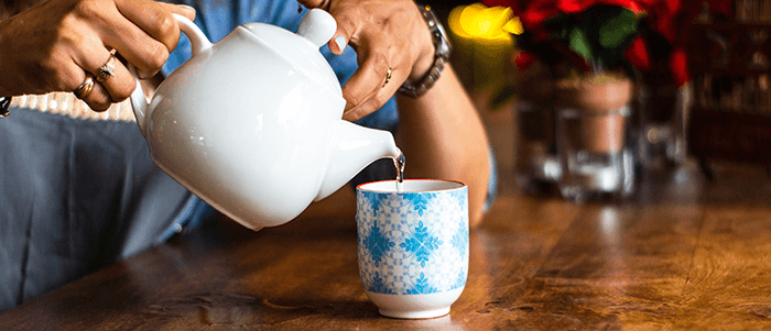 personne versant de la tisane dans une tasse à l'aide d'une théière