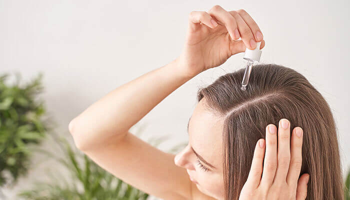 femme appliquant un médicament anti-chute sous forme de sérum sur ses cheveux