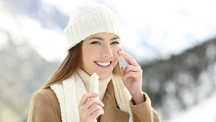 femme appliquant de la creme hydratante sur son visage en hiver