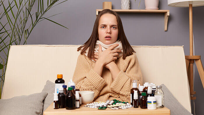 femme atteinte d'une agine assise sur son canapé face à des médicament contre le mal de gorge