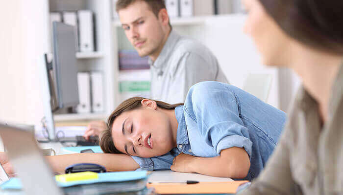 femme endormi sur son bureau entre ses collègues