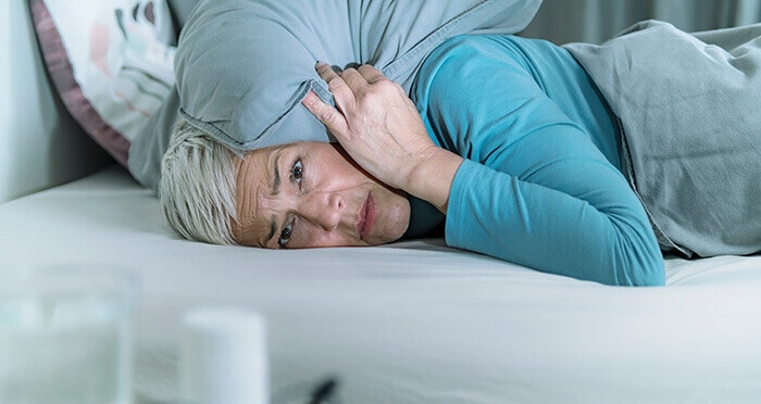 femme misophone, couchée dans son lit avec un coussin sur l'oreille