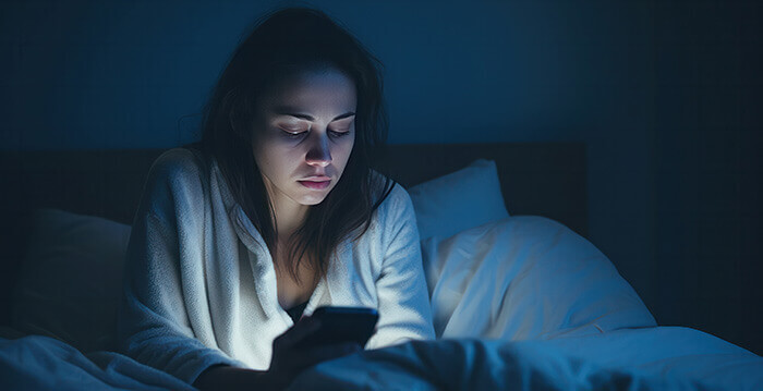 femme à l'air triste utilisant son mobile en plein milieu de la nuit dans son lit