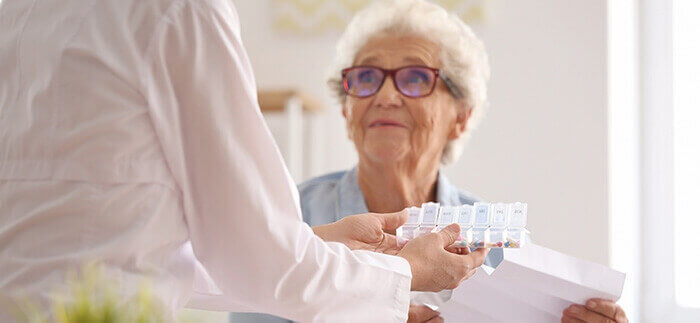 dame âgée recevant un pilulier et une série de recommandations d'une infirmière