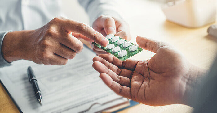 main d'un médecin tendant une plaquette de médicaments en expliquant la posologie