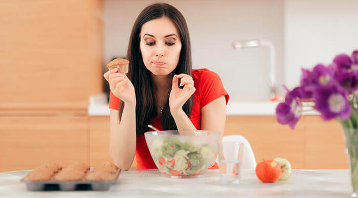 femme tiraillée entre une salade et des muffins