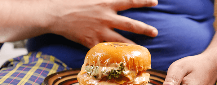 personne se tenant le ventre avec un burger en premier plan