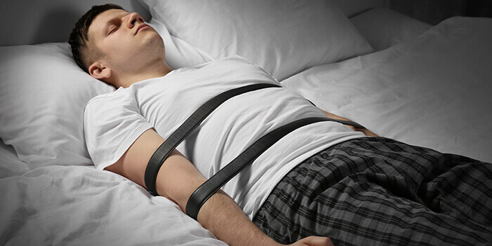 homme entravé sur un lit illustrant un épisode de paralysie du sommeil