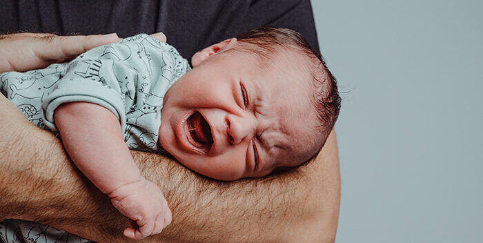 bébé qui pleur à gorge déployée dans les bras de son papa