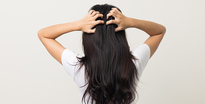femme de dos se grattant le cuir chevelu