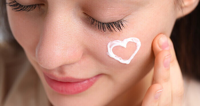 crème hydratante formant un coeur sur la joue d'une femme