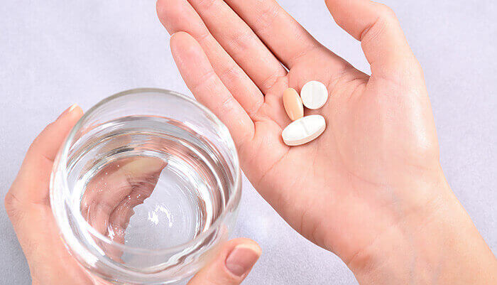 cachets anti-inflammatoires dans une main et verre d'eau dans l'autre