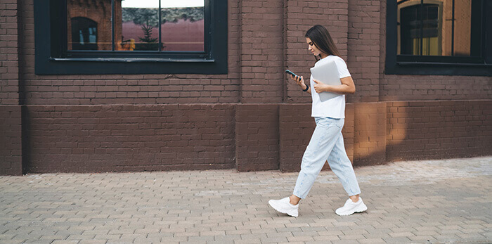 jeune femme se promenant en regardant son smartphone pendant sa pause déjeuner