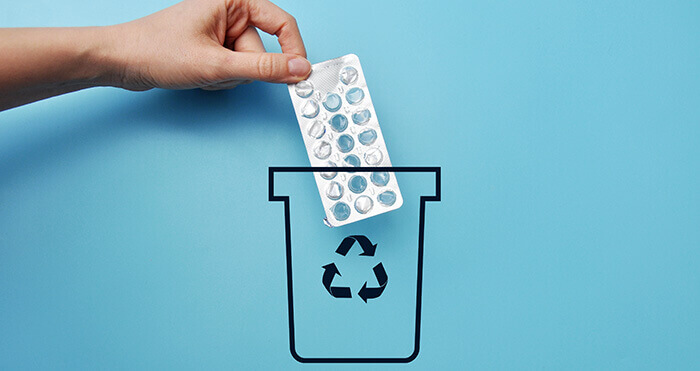personne jetant une plaquette de médicaments périmés dans une poubelle portant le logo recyclage