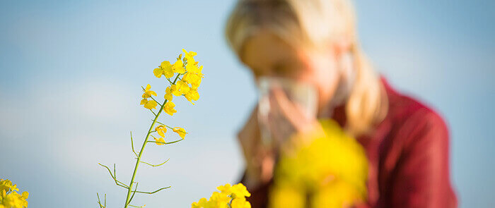 femme souffrant d'un rhume allergique avec des fleurs allergènes en premier plan