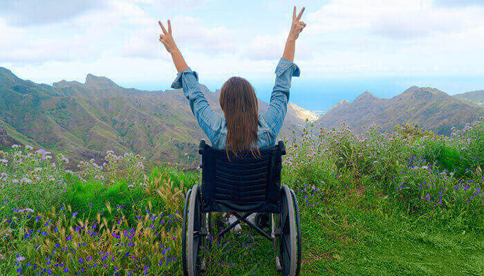 femme en fauteuil roulant levant les bras face à un beau paysage de nature