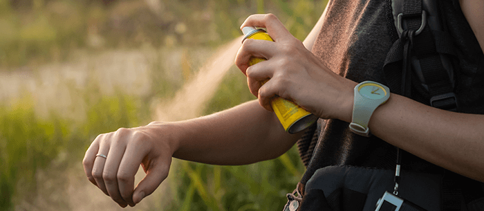 personne aspergeant son bras de répulsif anti-moustique