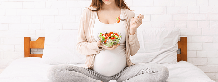 femme enceinte en tailleur mangeant un bol de légume