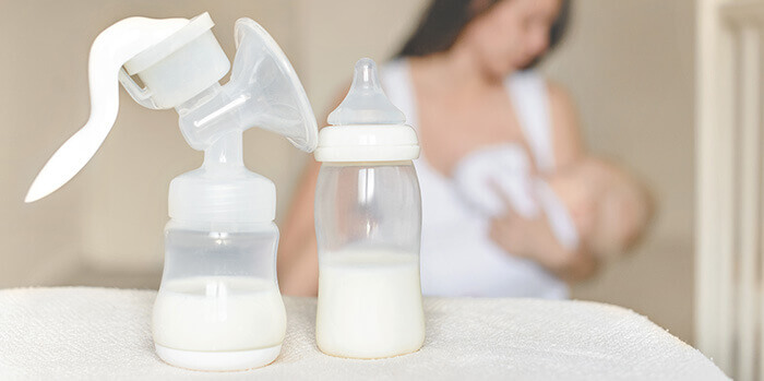biberon contenant du lait maternel au premier plan avec une maman allaitant son bébé dans le fond