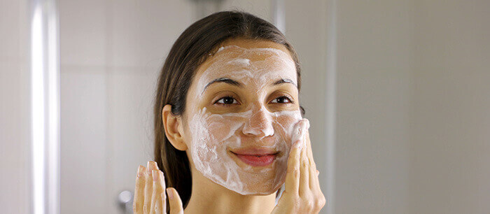 femme se nettoyant la peau du visage à l'aide d'une mousse nettoyante