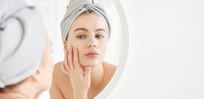 femme regardant sa peau de près dans un miroir