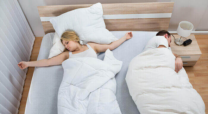 couple qui utilise des couettes séparées dans le lit