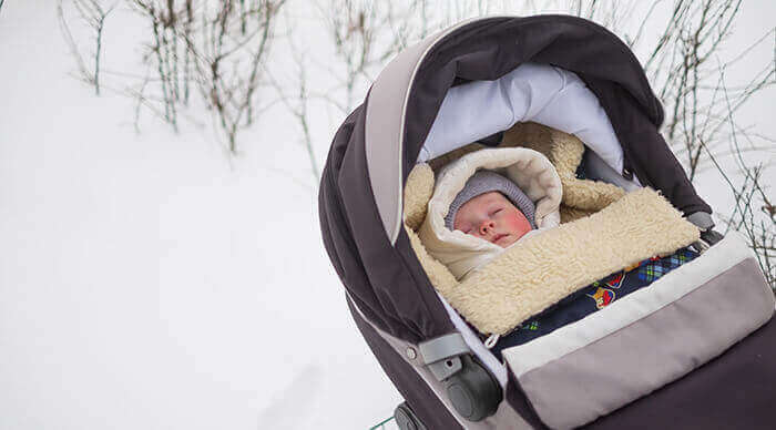 bébé faisant uen sieste dans une poussette à l'extérieur dans la neige