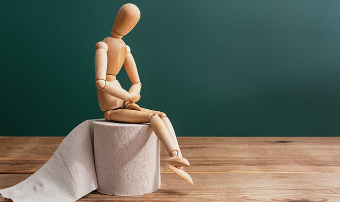 petit bonhomme de bois se tenant le ventre, assis sur un rouleau de papier toilette