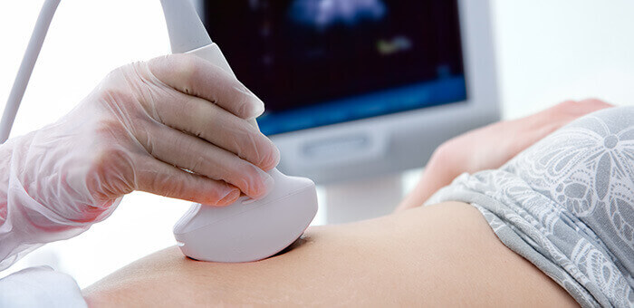 plan sur la sonde echographique posée sur le ventre d'une femme enceinte avec l'écran en arrière plan