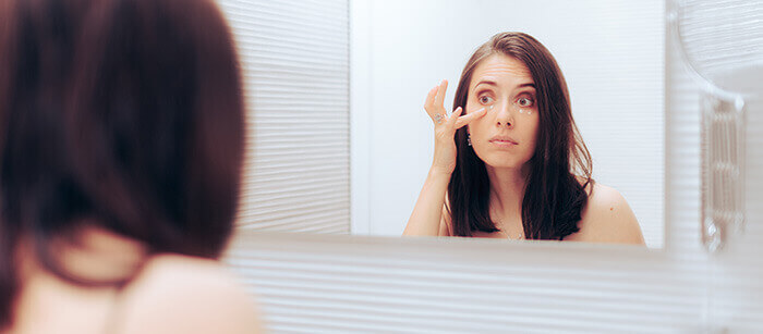 femme s'appliquant de l'anticerne devant un miroir