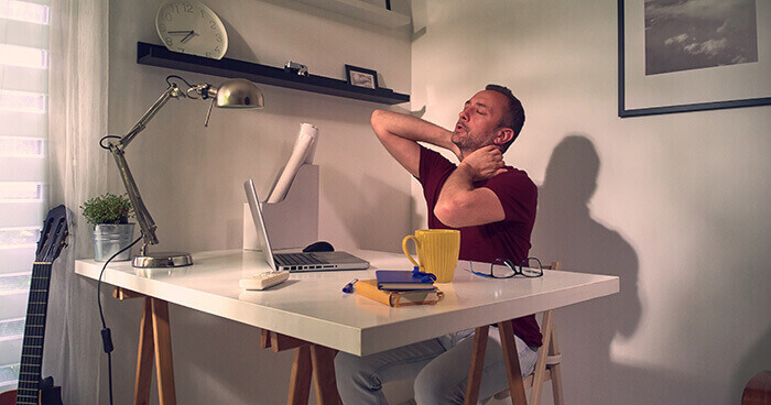 homme se massant la nuque à son bureau face à son ordinateur