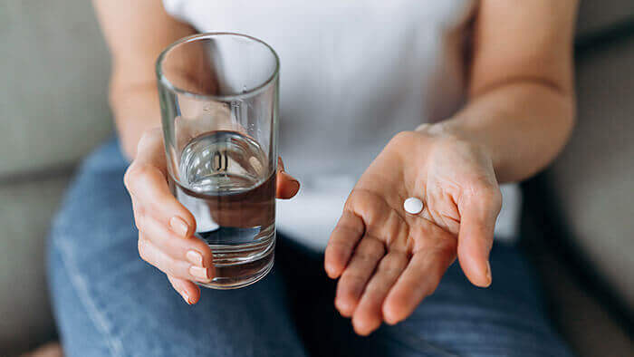 plan sur les mains d'une femme tenant un comprimé de paracétamol dans l'une et un verre d'eau dans l'autre