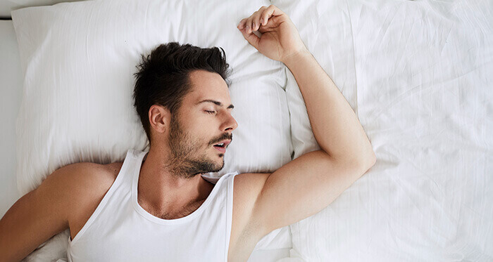 homme couché sur le dos dans un lit, ronflant la bouche ouverte