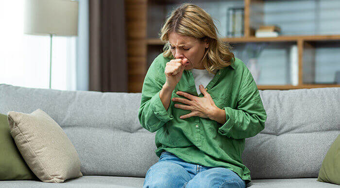 femme qui tousse en se tenant la poitrine, assise sur un canapé
