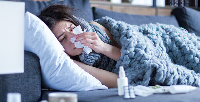 femme malade se mouchant couchée sur un canapé