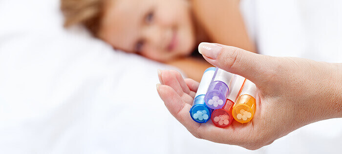 petite fille en fond avec une main tenant des tubes d'homéopathie en premier plan