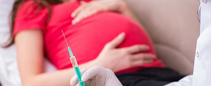 femme enceinte en second plan avec une seringue de vaccin en premier plan